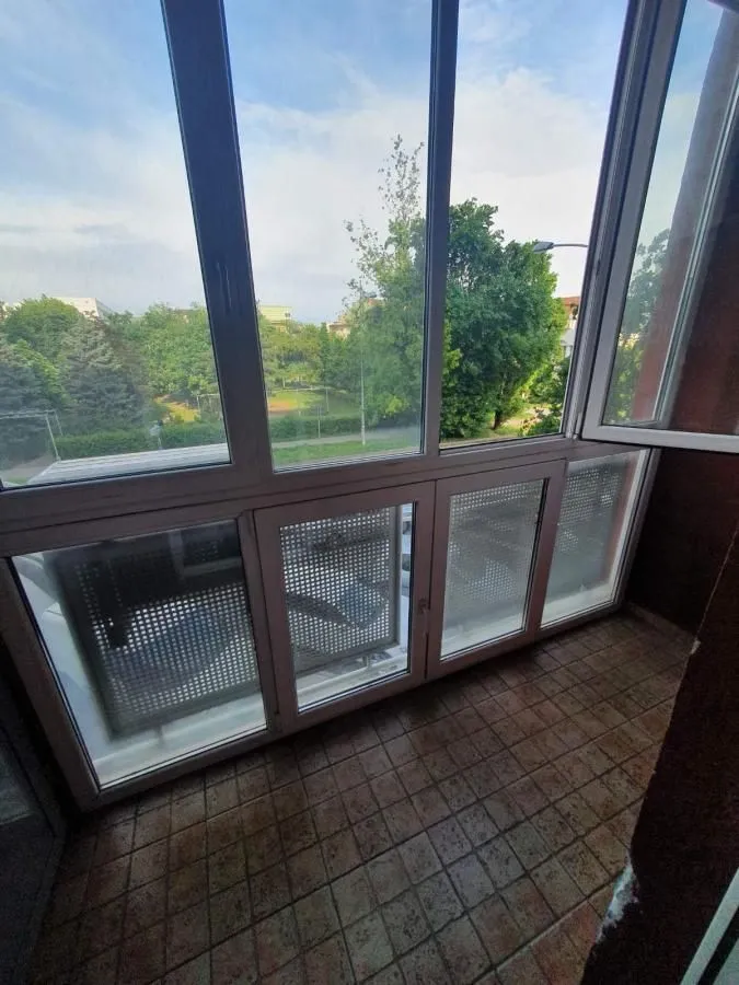 Zastakljeni balkon sa keramičkim pločicama na podu i pogledom na zelenilo.