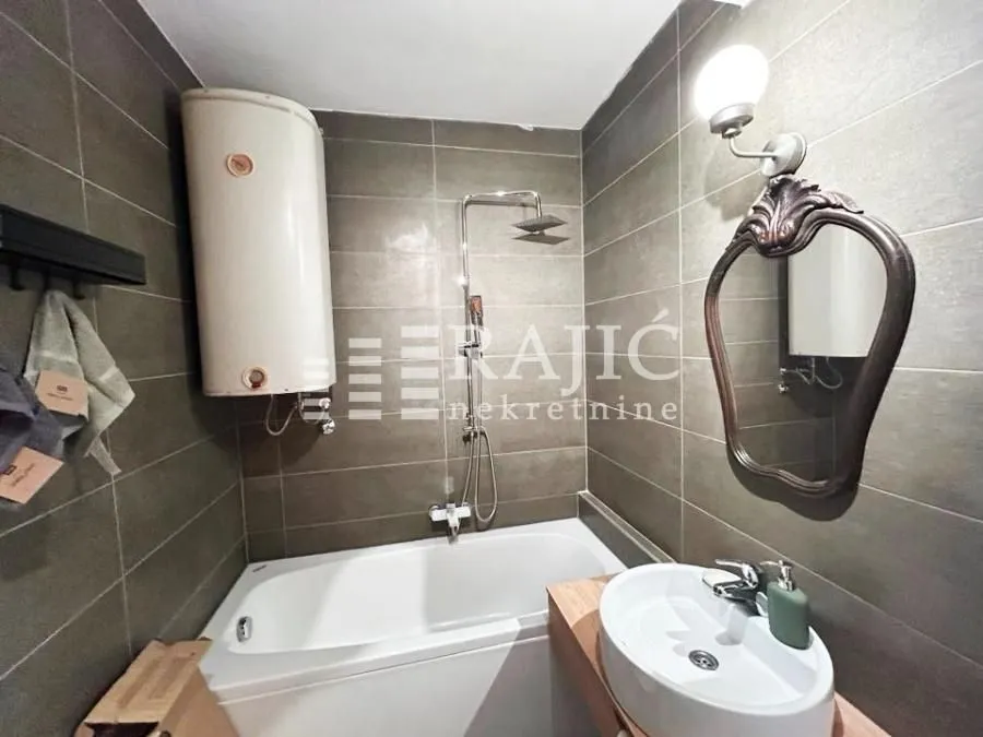 Small bathroom with a bathtub, sink, and water heater tiled with dark tiles.