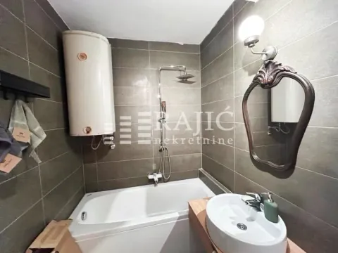 Small bathroom with a bathtub, sink, and water heater tiled with dark tiles. - image 6