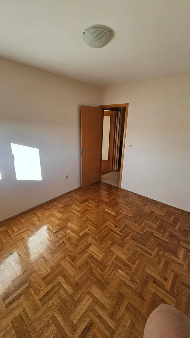 Prazna soba sa parketom i otvorenim drvenim vratima.