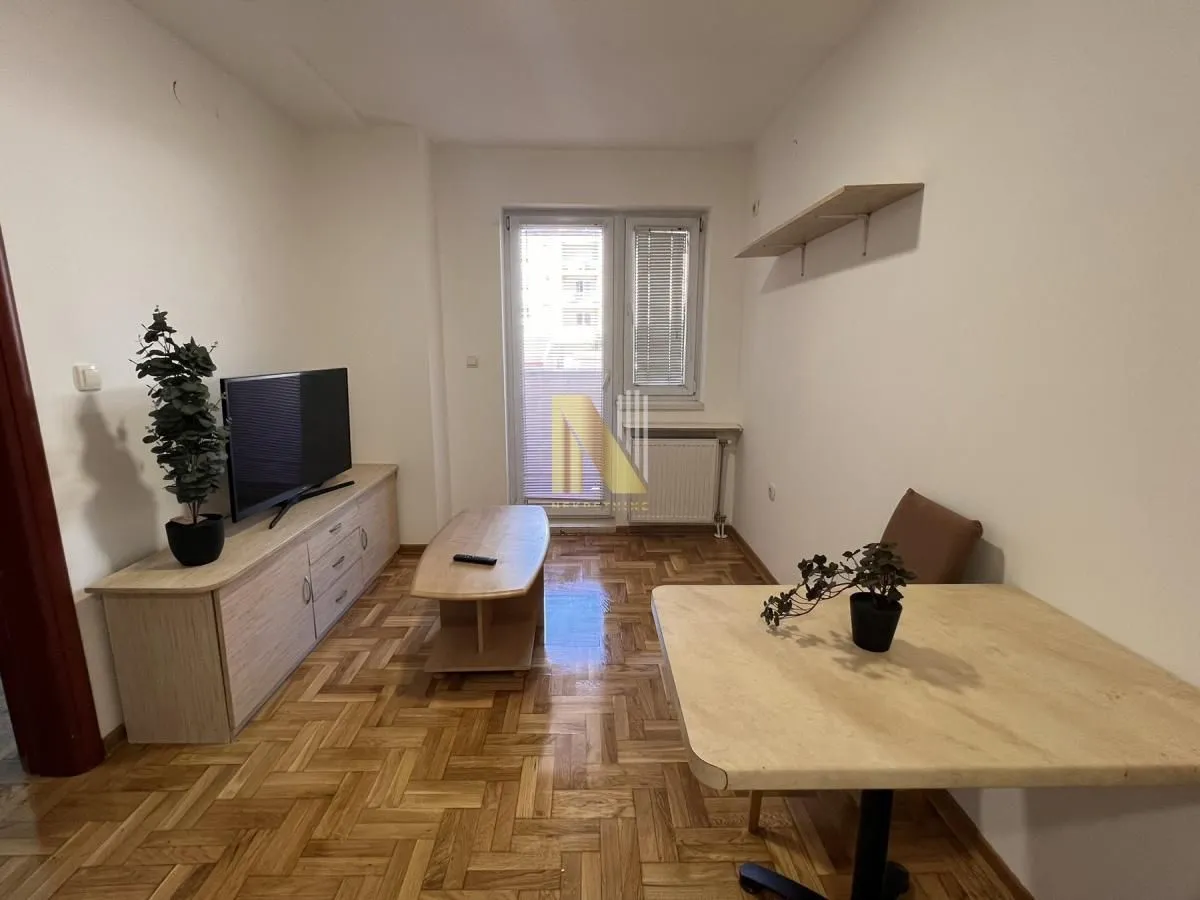 Manja dnevna soba sa drvenim parketom, televizorom i trpezarijskim stolom.