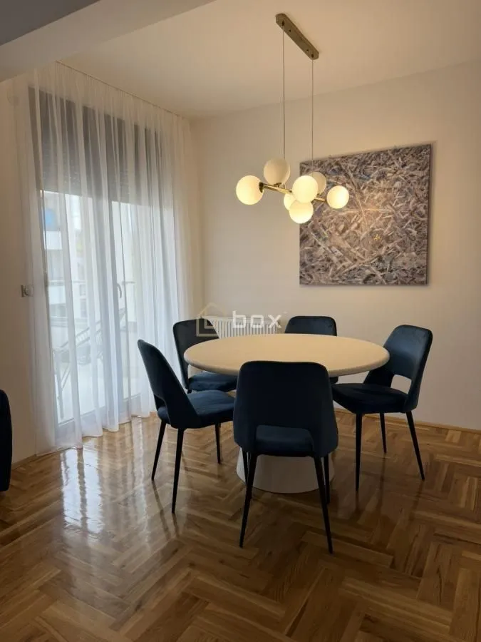 Trpezarija sa okruglim stolom, plavim stolicama i lusterom.