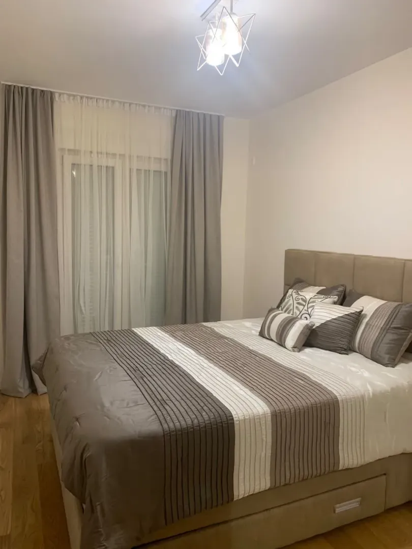 Uređena spavaća soba sa bračnim krevetom i prozorom sa zavjesama.