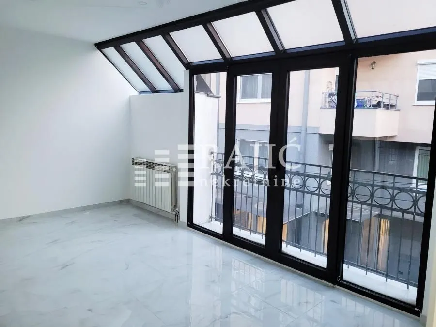 Empty room with light tiles and a large glass roof and windows.