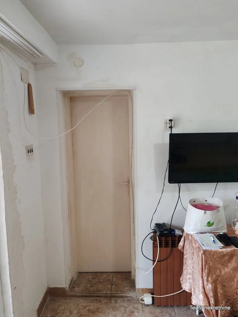 Pogled na bijeli zid sa sobni vratima, televizorom i radnim stolom.