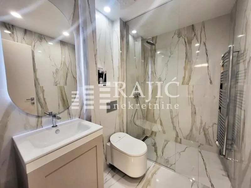 Modern bathroom with marble tiles, washbasin, and walk-in shower.