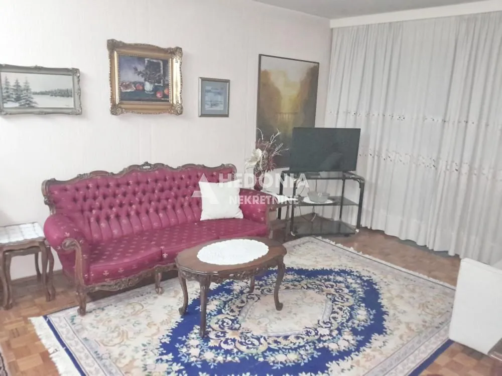 Dnevna soba sa garniturom, stočićem i slikama na zidu.