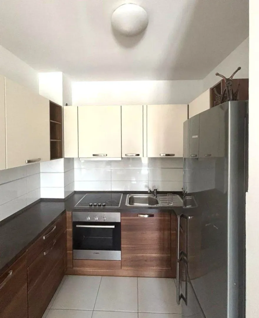 Compact kitchen with wooden cabinetry, white upper cabinets, and built-in appliances.