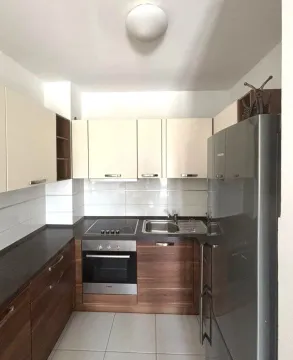 Compact kitchen with wooden cabinetry, white upper cabinets, and built-in appliances. - image 6