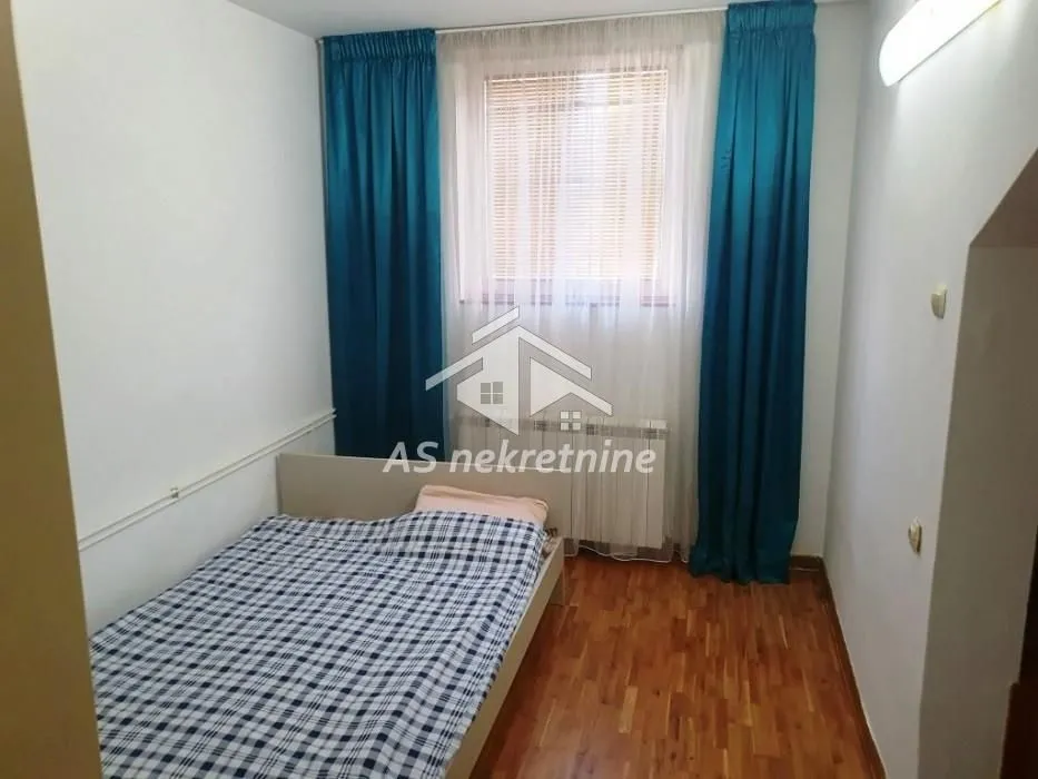 Smaller bedroom with a bed and a window with blue curtains.