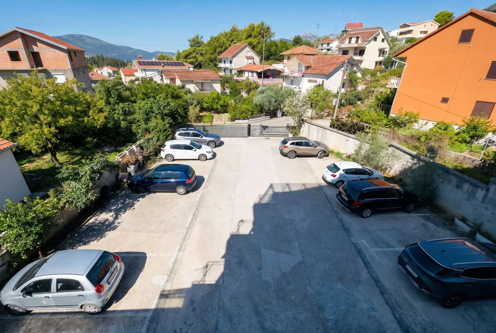 Pogled na parking prostor ispred zgrade sa parkiranim automobilima.