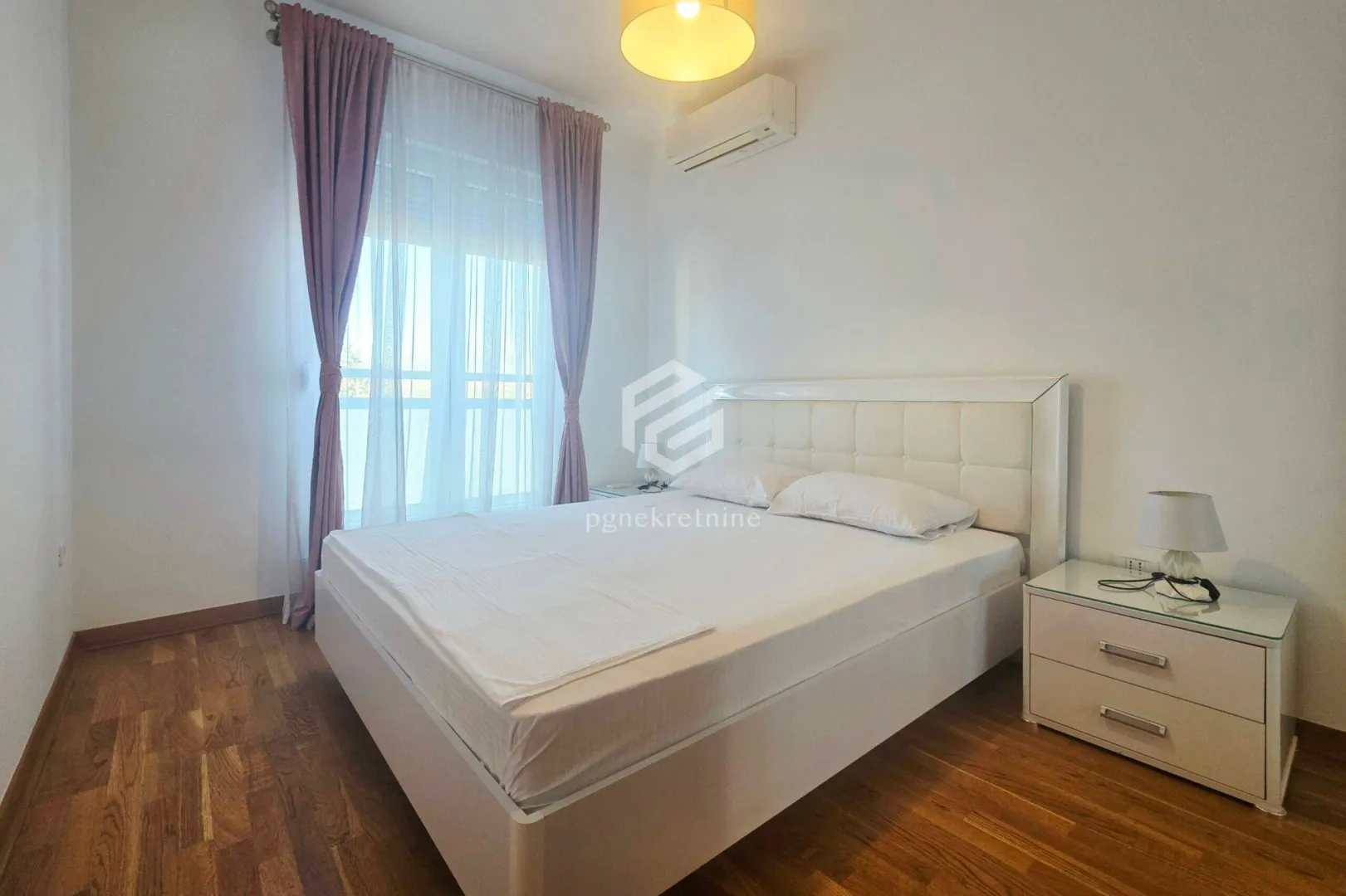 Bright bedroom with a white bed, nightstand, and window with curtains.
