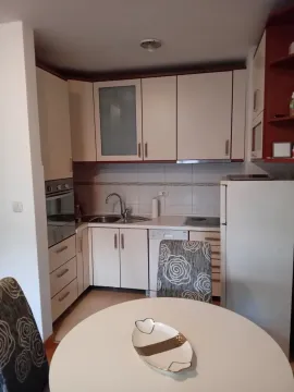 Small kitchen with white cabinets, a sink, built-in appliances, and a dining table in the foreground. - image 8