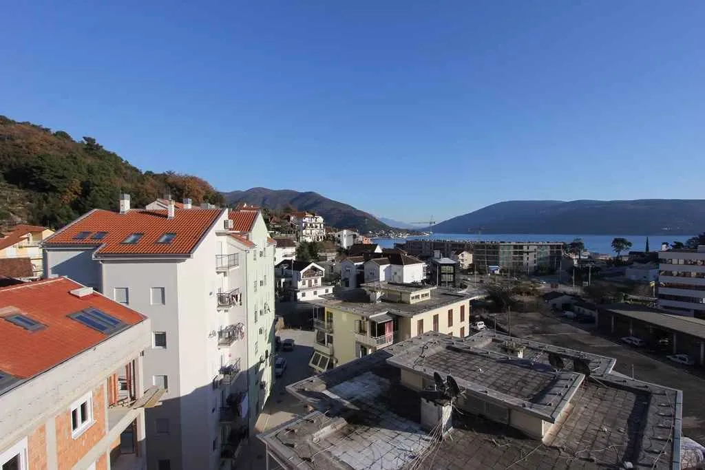 Pogled sa visine na stambene zgrade, more i planine u daljini.