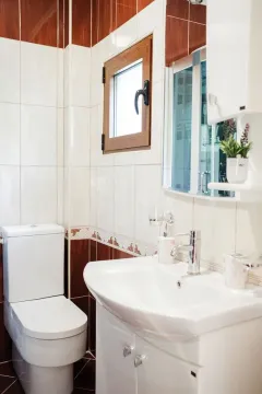 A compact bathroom featuring a white sink, toilet, and a combination of white and brown wall tiles. - image 18