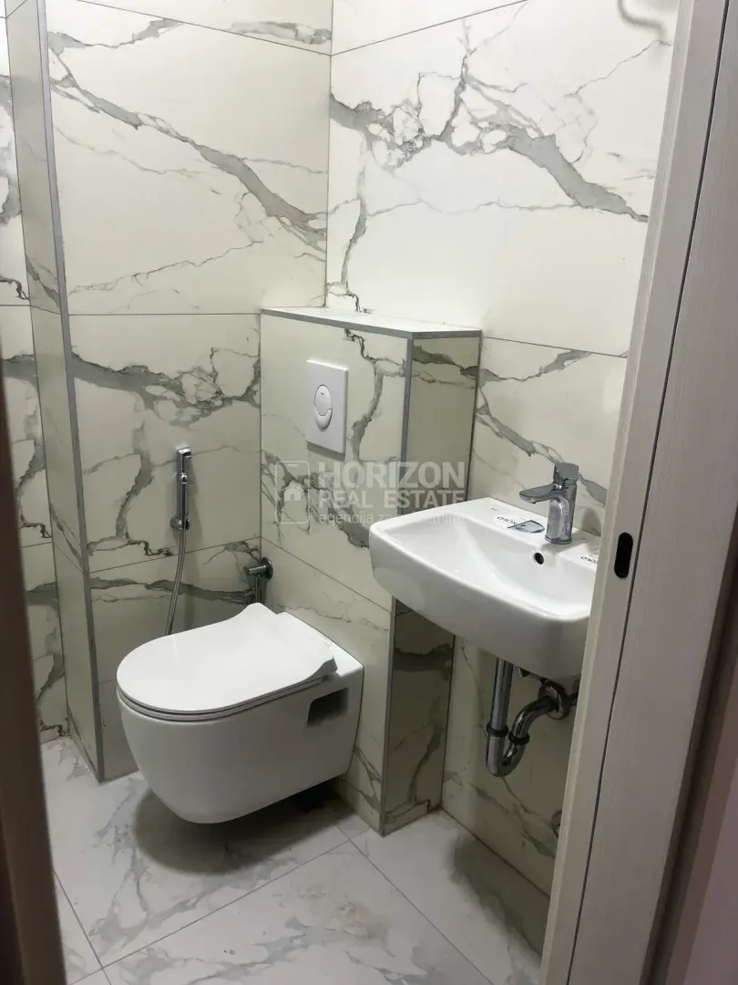 Small bathroom with modern marble tiles, toilet and washbasin.
