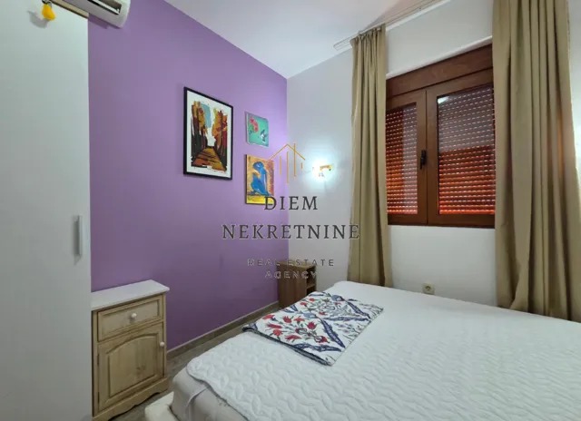 Small bedroom with a bed, purple accent wall, and a window with curtains.