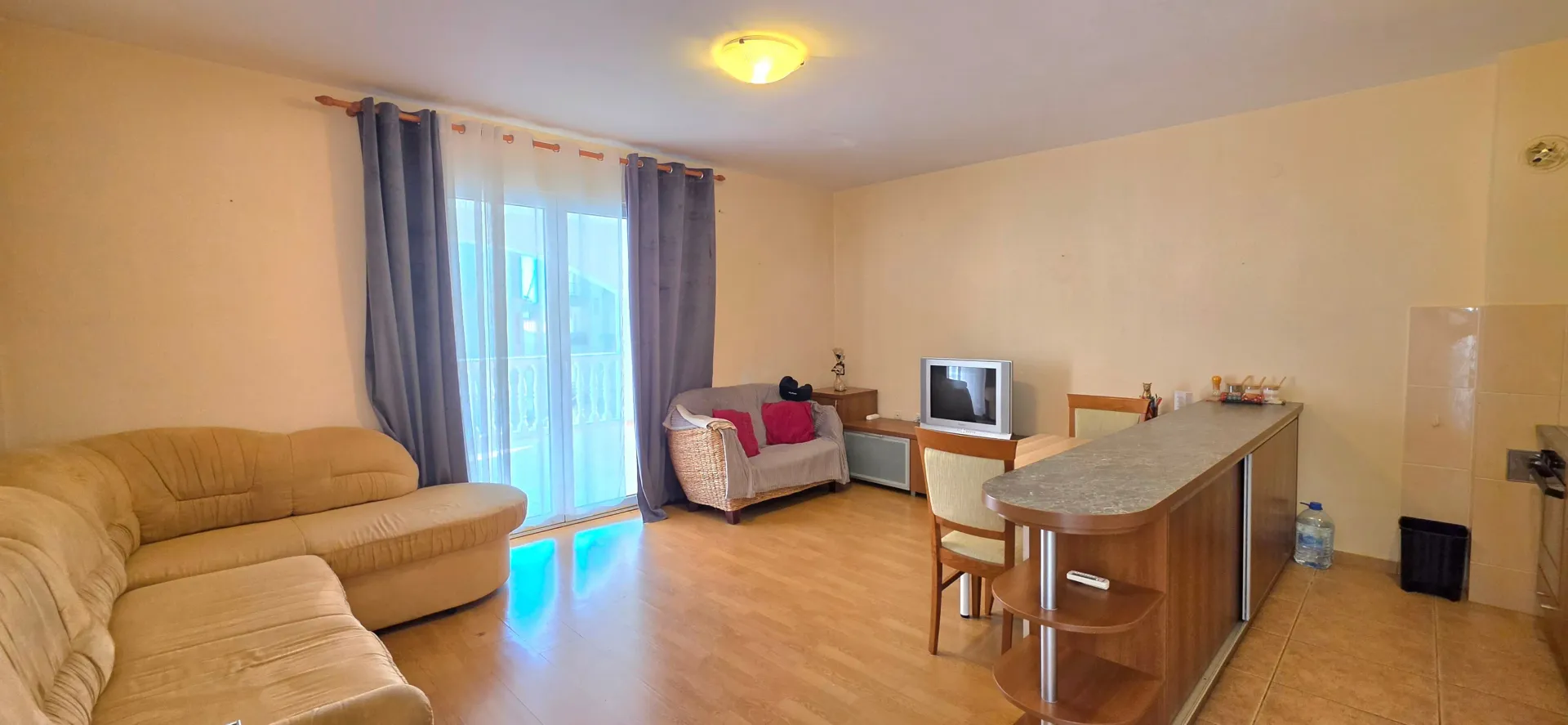 Dnevni boravak sa garniturom, trpezarijskim stolom i kuhinjskim šankom.