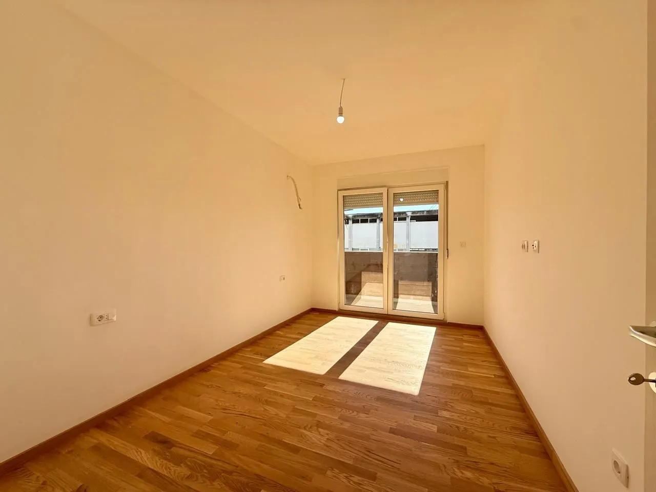 Prazna soba sa drvenim podom i izlazom na terasu.