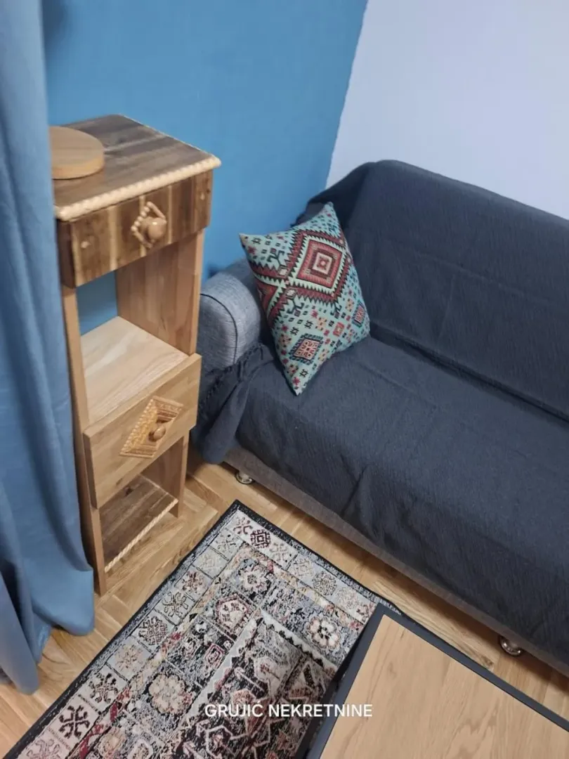 Part of the living room with a sofa, a wooden side table, and a rug.