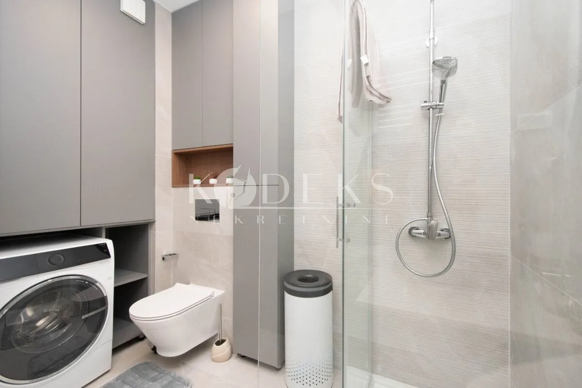 Moderne kupatilo sa tuš kabinom, wc šoljom i ugrađenom mašinom za pranje veša.