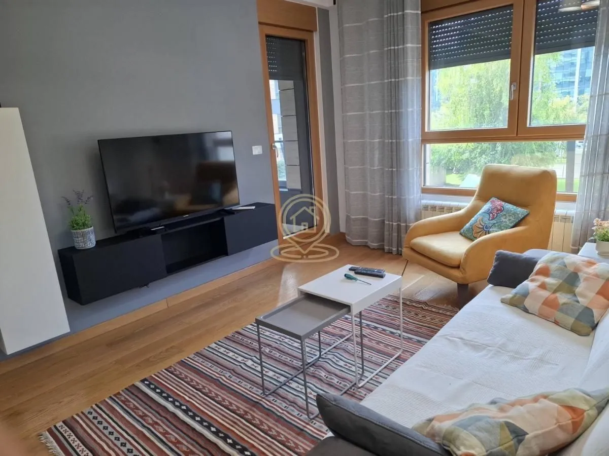 Dnevna soba sa garniturom, foteljom, televizorom i trpezarijskim stolom.