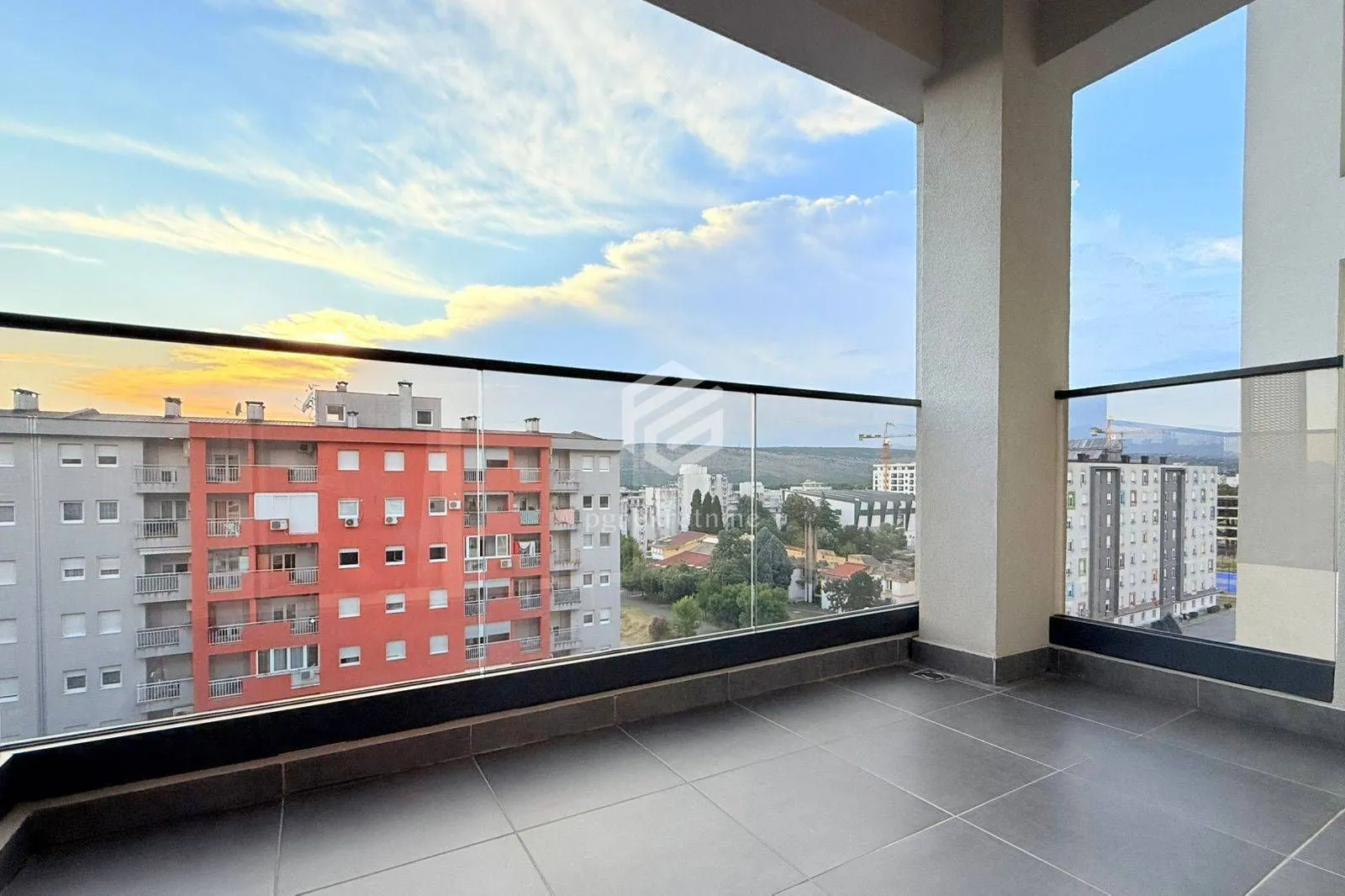 Prostrani balkon sa staklenom ogradom i pogledom na grad.