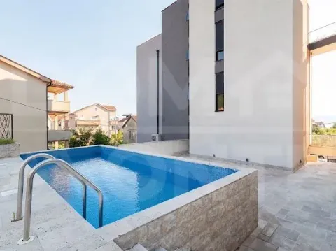 Spoljašnji bazen sa popločanim platoom ispred moderne zgrade. - image 16