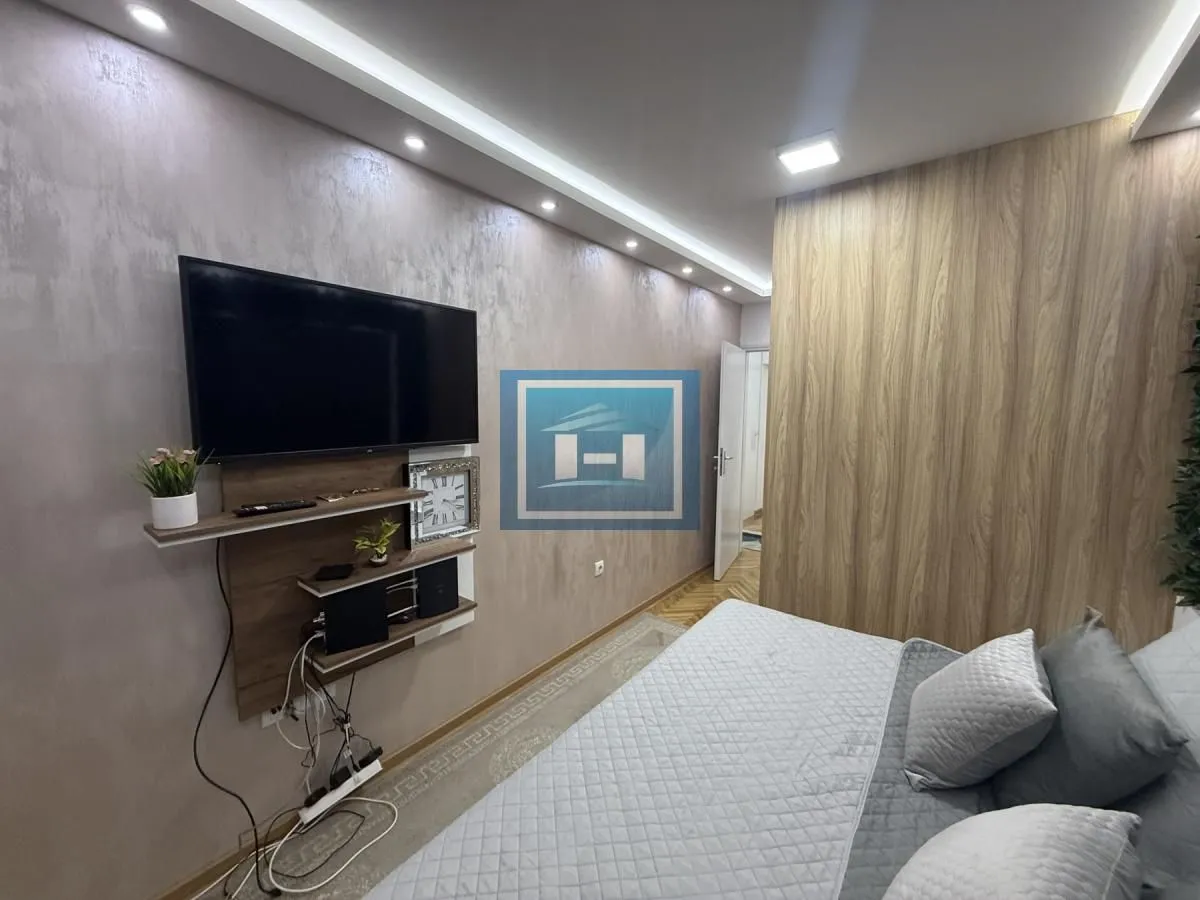 Nameštena spavaća soba sa bračnim krevetom, TV-om i drvenim zidnim oblogama.