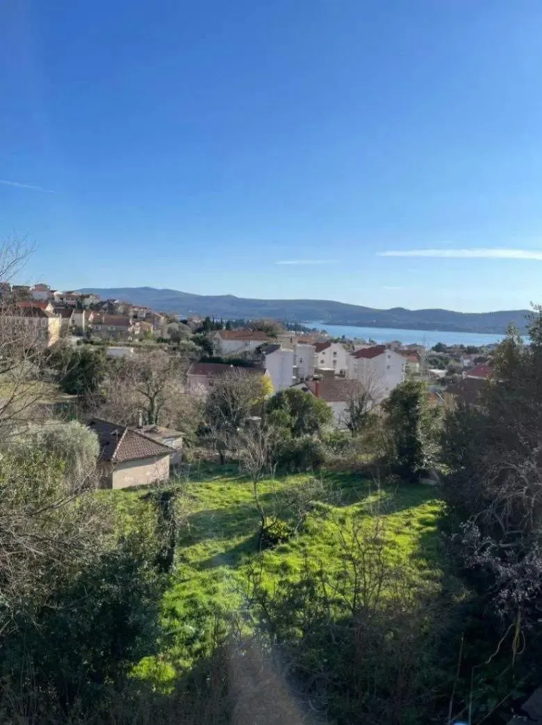 Pogled sa nekretnine na naselje, zelenilo i more u daljini.