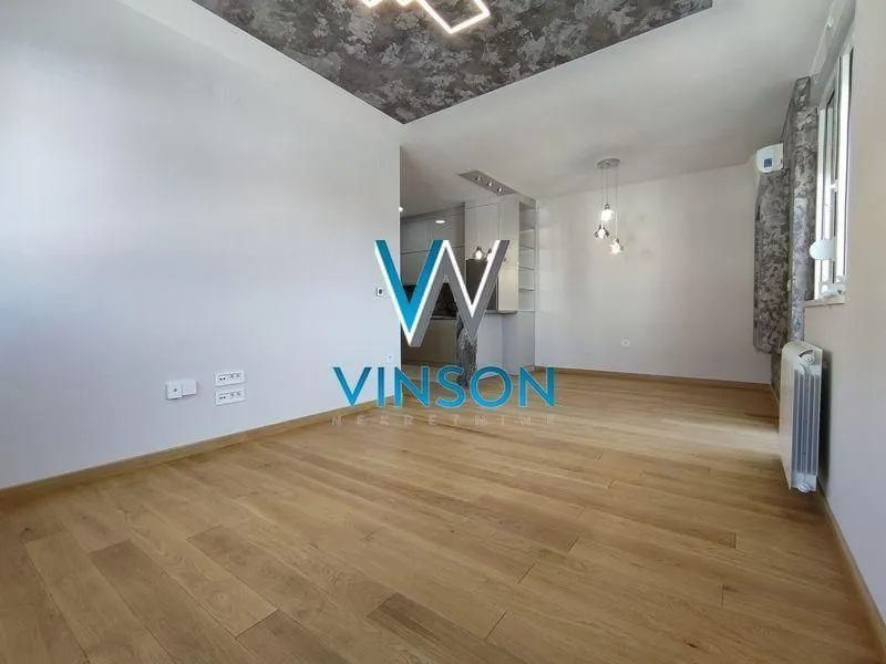 Empty living room with wooden flooring and a view of the kitchen.