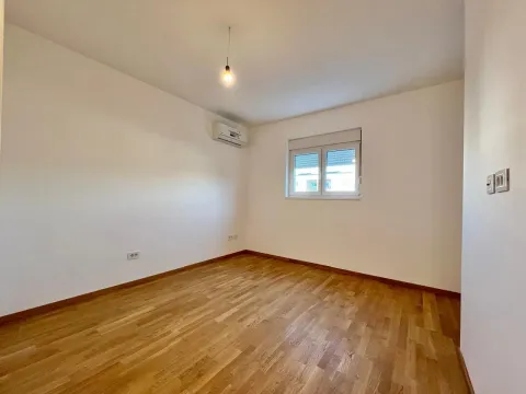 Prazna soba sa parketom, bijelim zidovima, klima uređajem i prozorom. - image 7