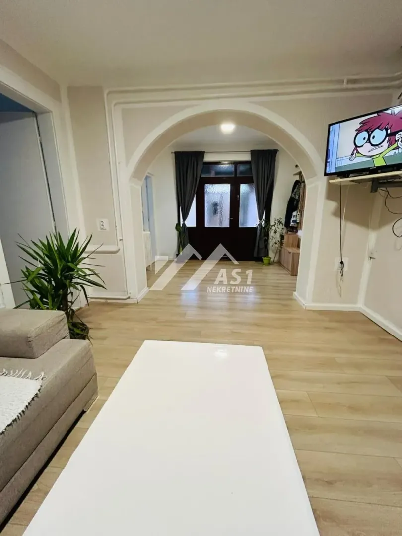 Dnevna soba sa garniturom, televizorom i pogledom prema ulaznim vratima.