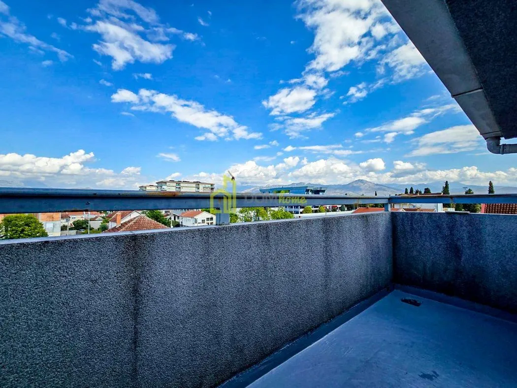 Otvoreni balkon sa pogledom na okolnu četvrt i planine u pozadini.
