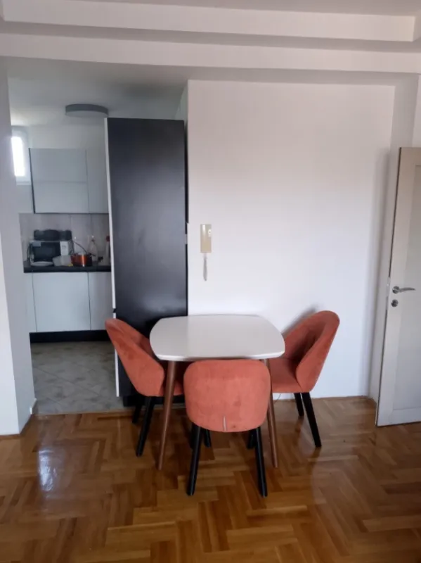 Trpezarijski sto sa četiri stolice i pogledom na kuhinju u pozadini.