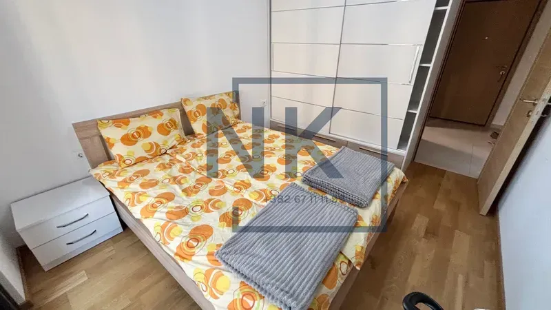 Namještena spavaća soba sa bračnim krevetom, bijelim garderoberom i noćnim stočićem.
