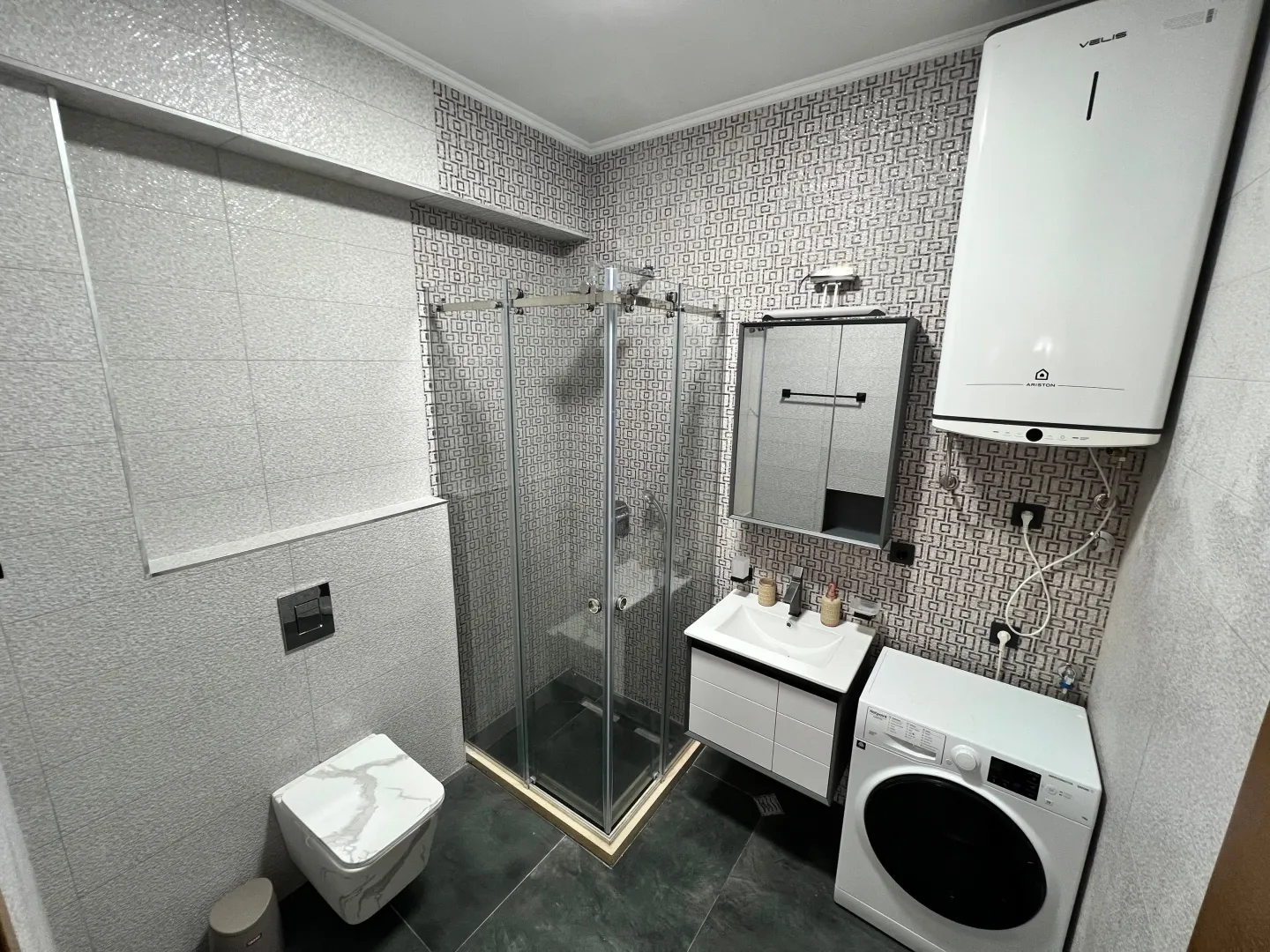 Modern bathroom equipped with a shower cabin, vanity unit, and washing machine.