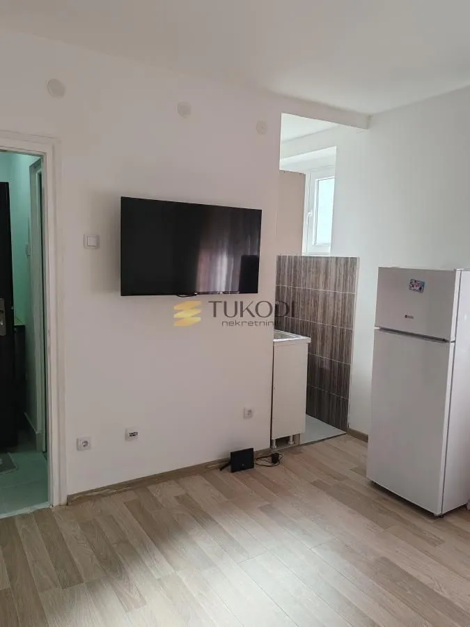 Living room with a wall-mounted TV and a refrigerator.