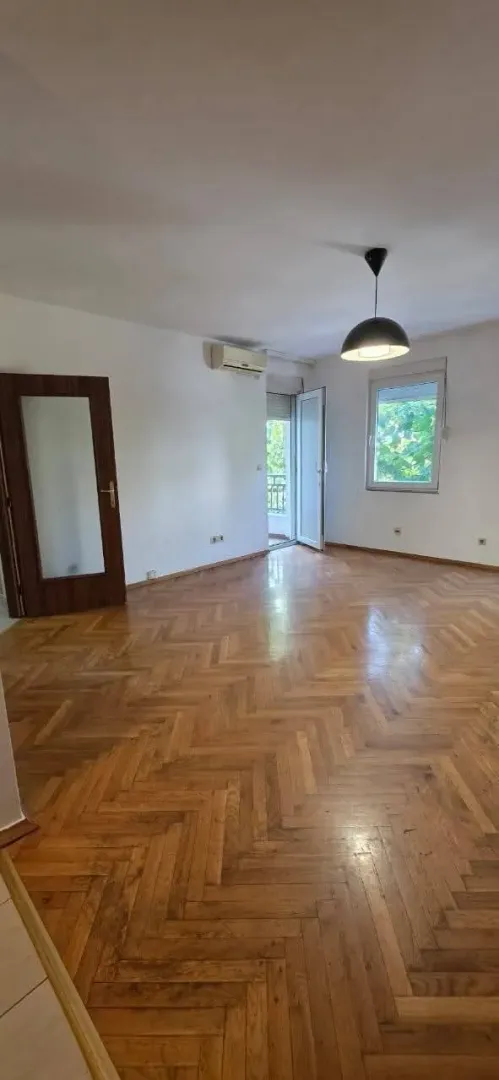 Prazna dnevna soba sa parketom i izlazom na terasu.