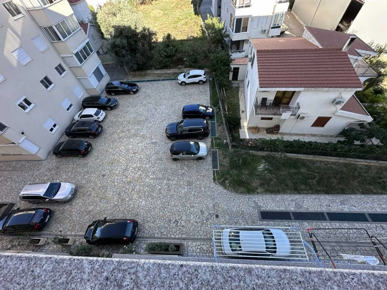 Pogled odozgo na parking prostor sa parkiranim automobilima i okolnim zgradama.