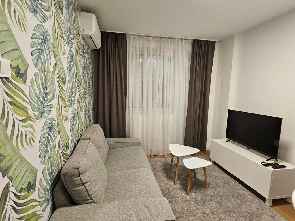 Dnevna soba sa garniturom, televizorom i tapetom sa motivom lista.