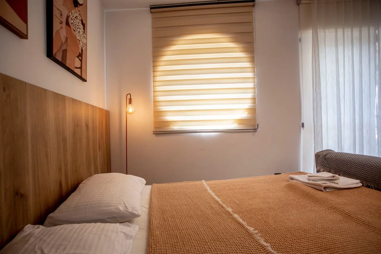 A furnished bedroom with a double bed and a window with blinds.