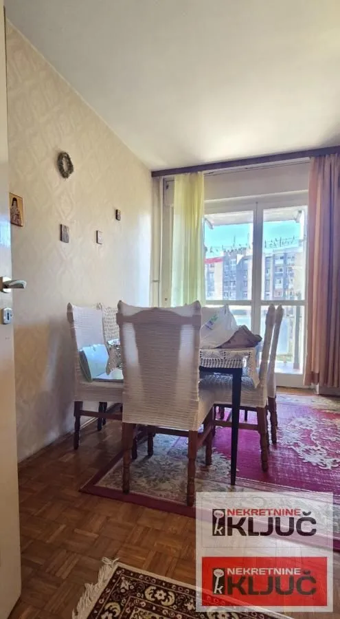 Trpezarija sa stolom, stolicama i izlazom na balkon.