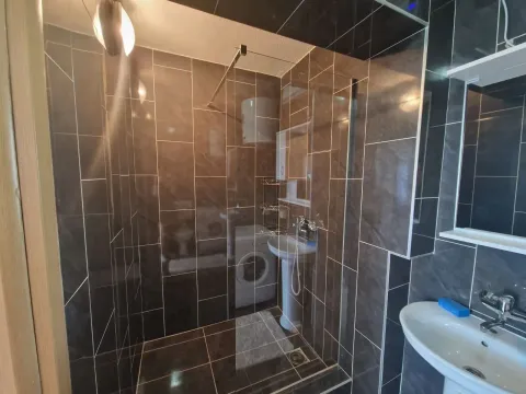 Bathroom with dark tiles, a glass walk-in shower, and a washbasin. - image 5