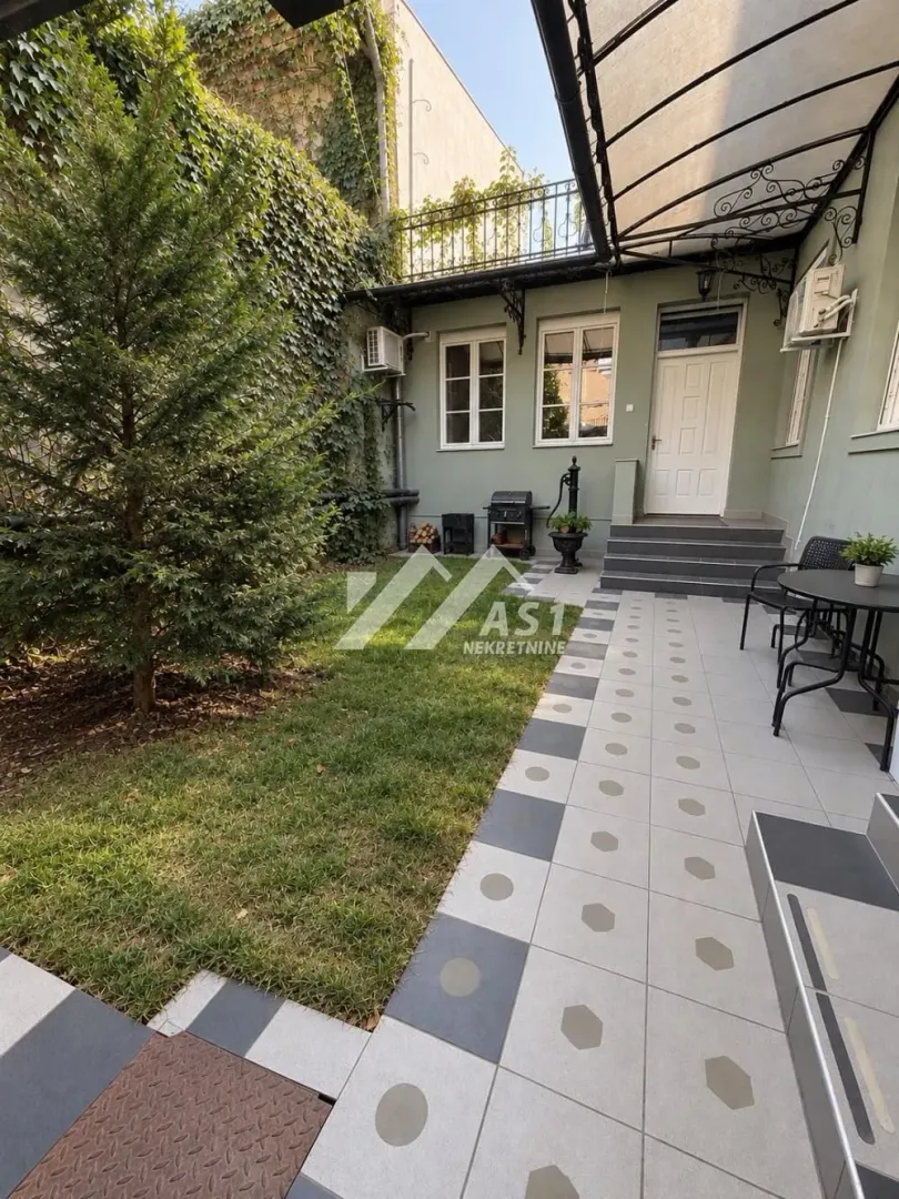 Landscaped courtyard with a lawn, trees, and a tiled area in front of the entrance.