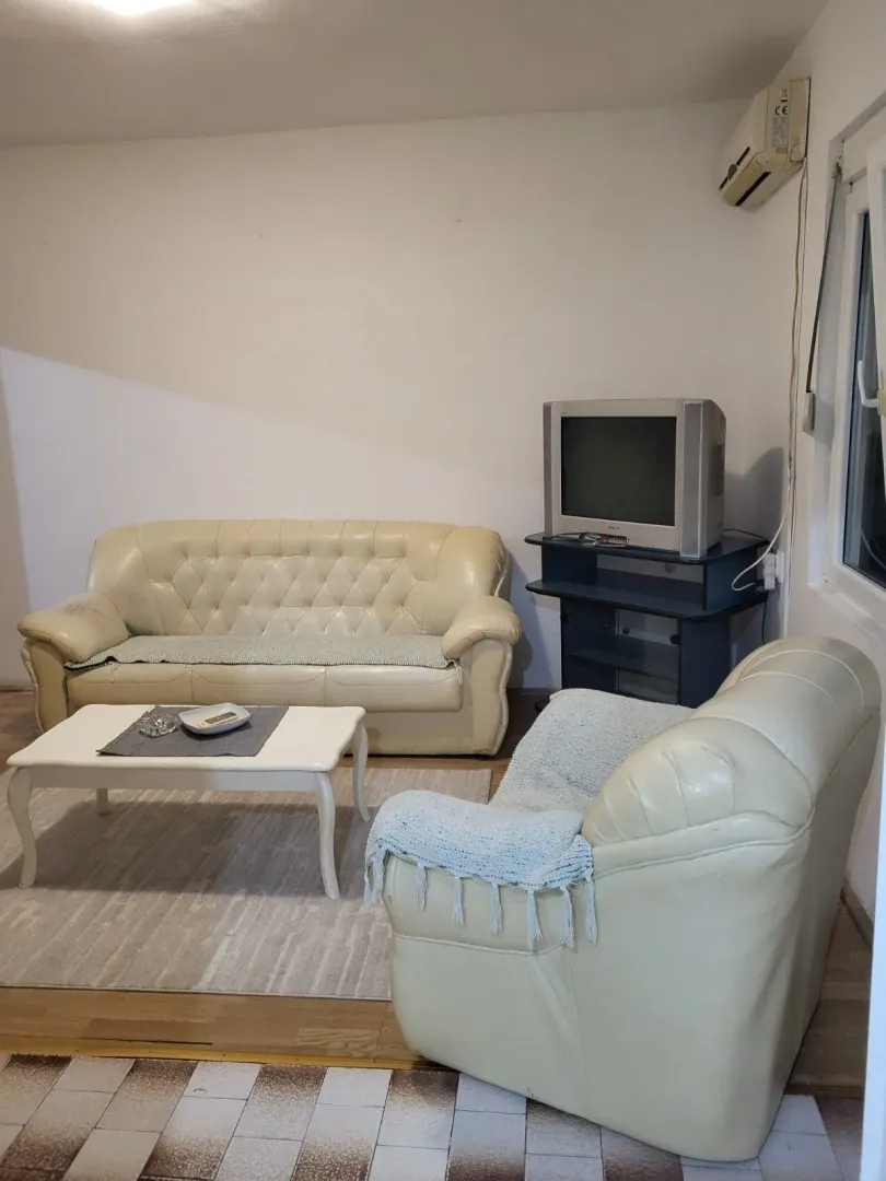 Dnevna soba sa kožnom garniturom, klub stolom i televizorom.