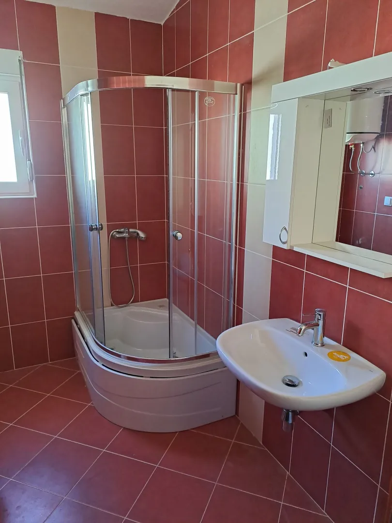 Kupatilo sa tuš kabinom, umivaonikom i ogledalom sa ormarićem.