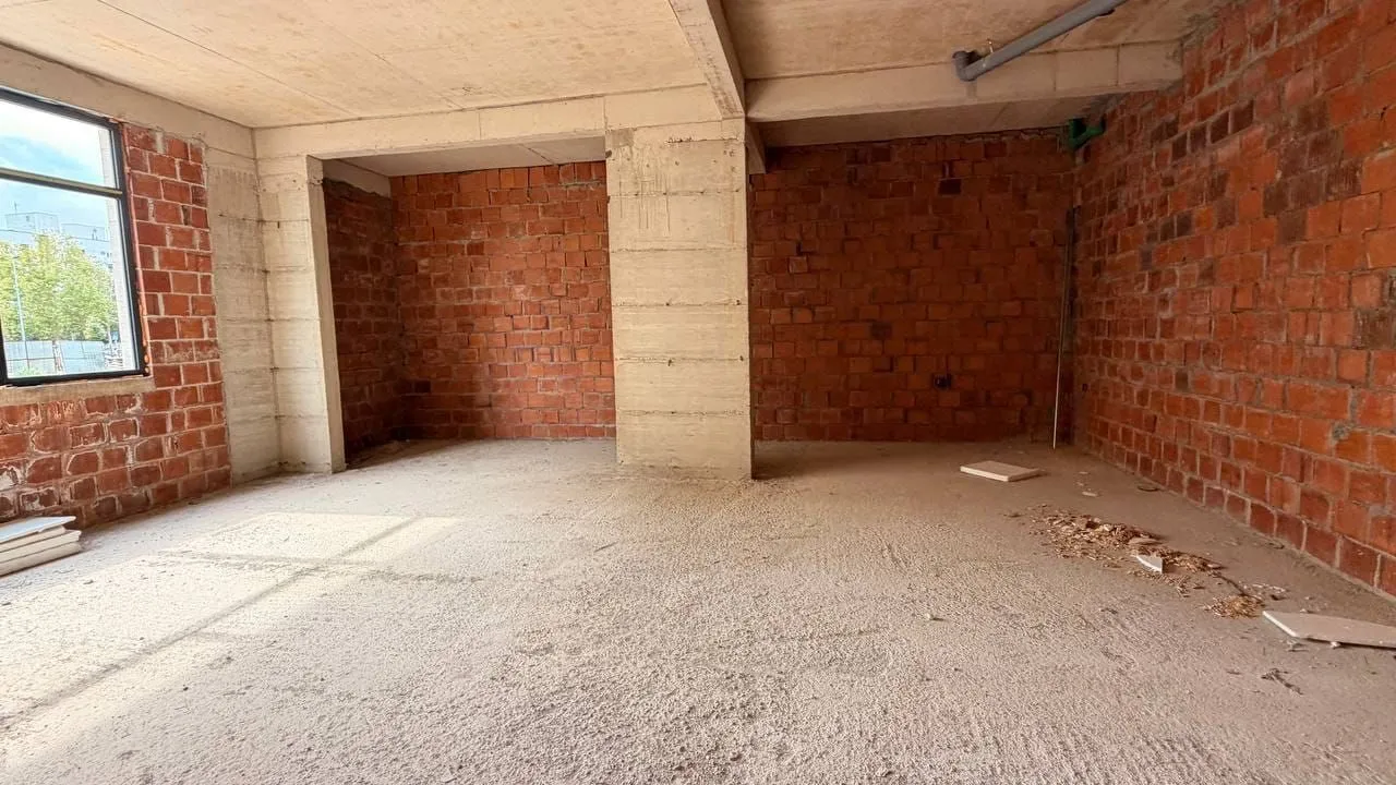 Interior of an unfinished raw space with concrete pillars and brick walls.