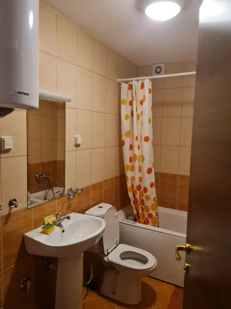 Manje kupatilo sa umivaonikom, WC šoljom i kadom sa šarenom zavjesom.