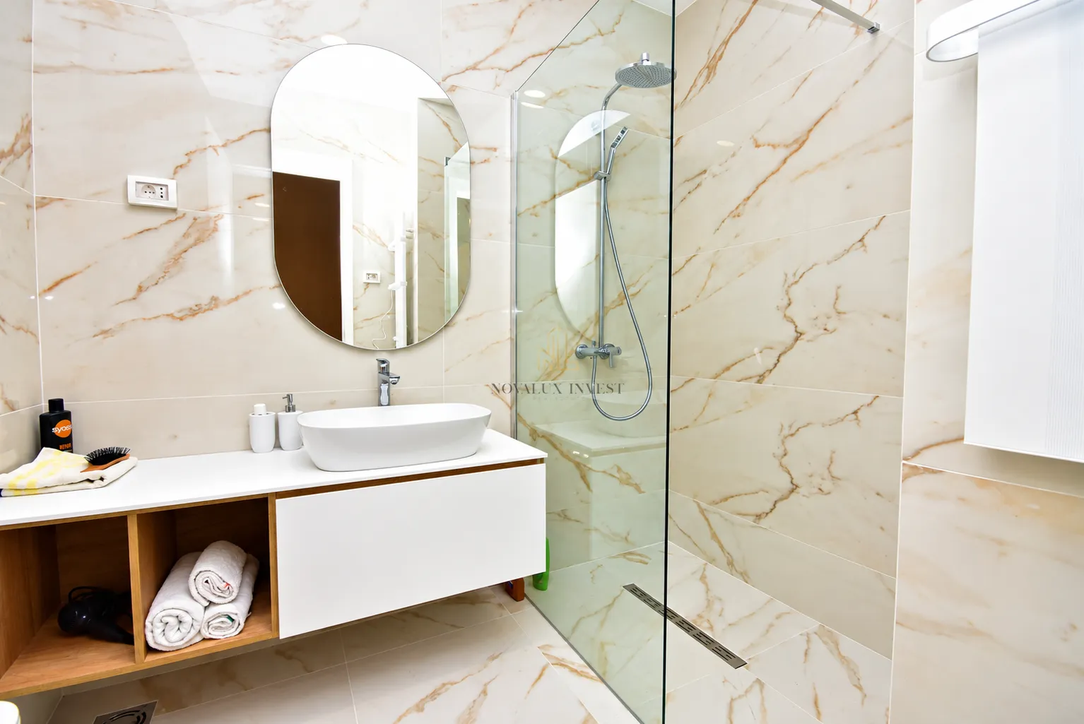 Modern bathroom with a washbasin, mirror, and walk-in shower finished with marble tiles.